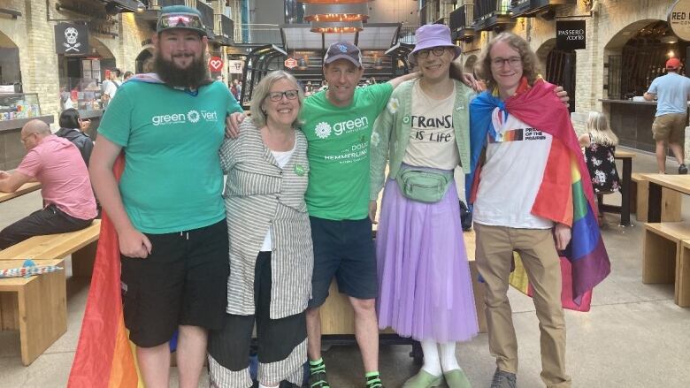 Five people, including two draped in rainbow Pride flags, pose for a photo at The Forks. 