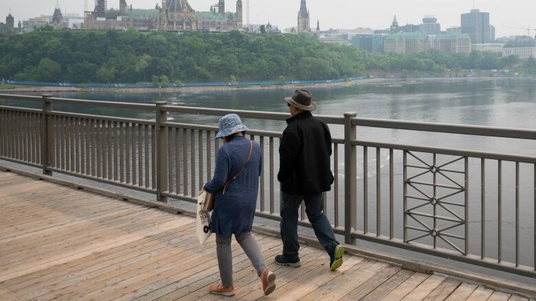 Two people walk a bridge between cities on a smoky day.