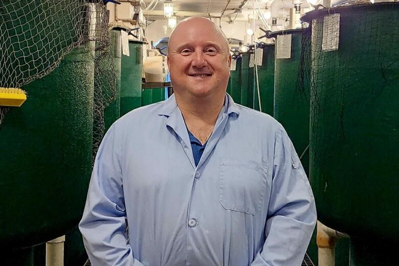 A man with no hair stands next to fish nets smiling. 