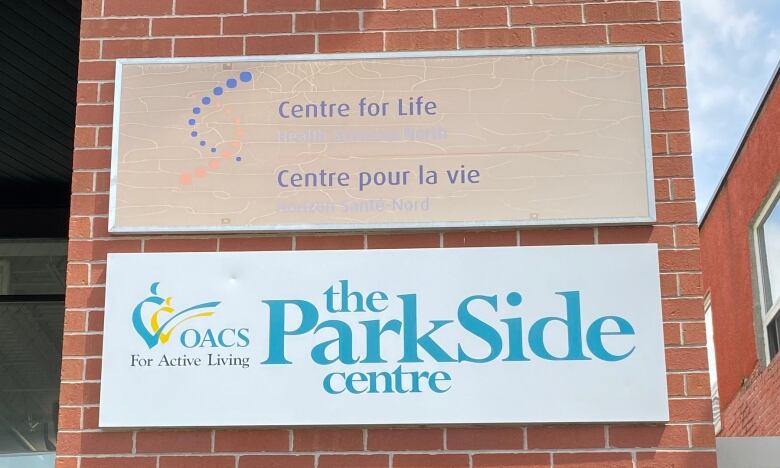 A grey building with a sign that is white and green in colour says parkside centre. In june the organization is hosting a food drive for seniors.