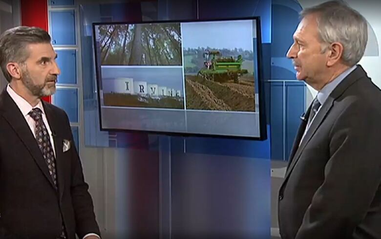 Two men standing facing each other with a TV screen behind them