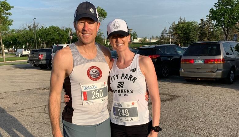 A man and woman in running gear pose for a photo, standing with their arms around each other.