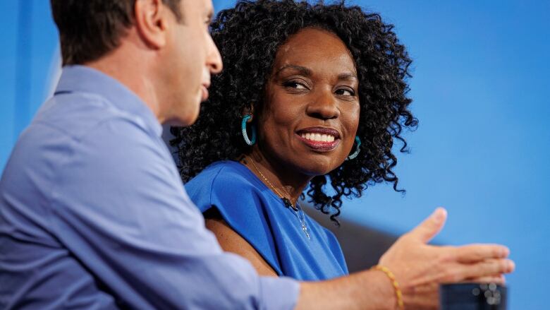 Man in a blue shirt talks beside a woman in a blue dress.