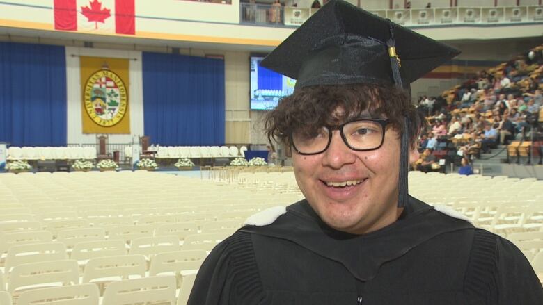 Tyrell Bird stands in the University of Manitoba auditorium wearing his graduation cap.  