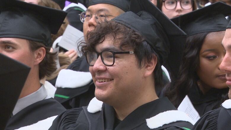 Bird and several other graduates sit waiting to be called on stage to receive their diplomas. 