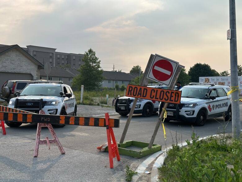 Three police cruisers behind a sign that says 