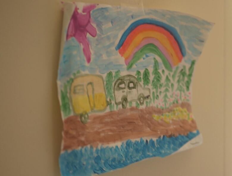 A child's drawing taped to a wall shows a car pulling a camper trailer in the woods under a rainbow.