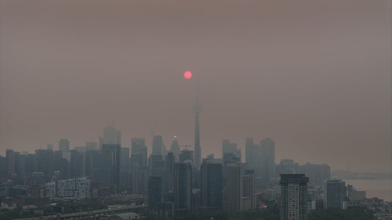 Smog lingers over Toronto at sunrise, with a red sun glowing behind the fog