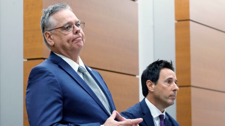 Two men in suits are shown standing inside a room.