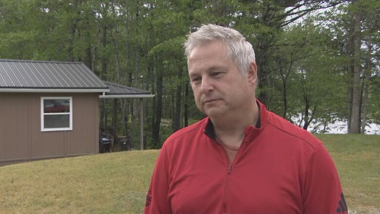 A man wearing a red sweater stands outside near a small cabin.