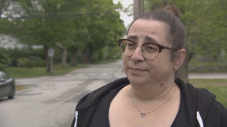 A woman wearing glasses stands outside and looks off camera.