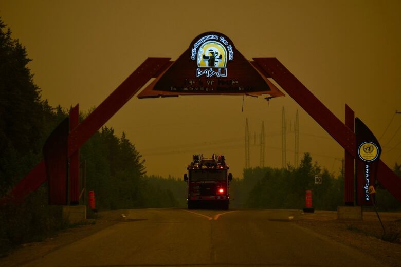 A fire truck surrounded by an orange, smoke filled sky at dusk drives on a gravel road. 