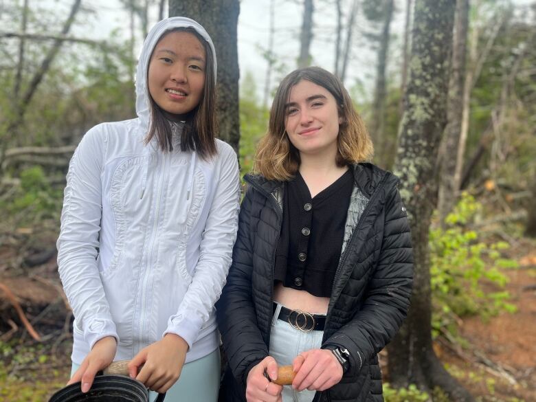 Two students stand side-by-side in the forest. One is in a white hoodie and the other a black puffer jacket. 