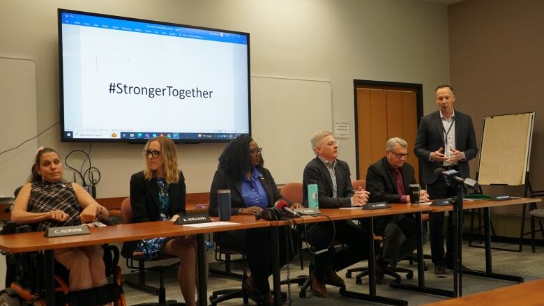 A row of six people sitting behind a desk.