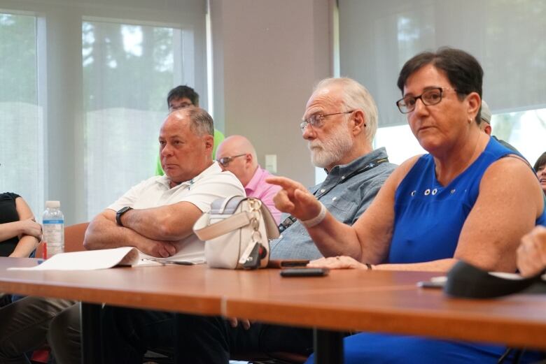 Three people sitting. One with his armed crossed and a woman pointing.