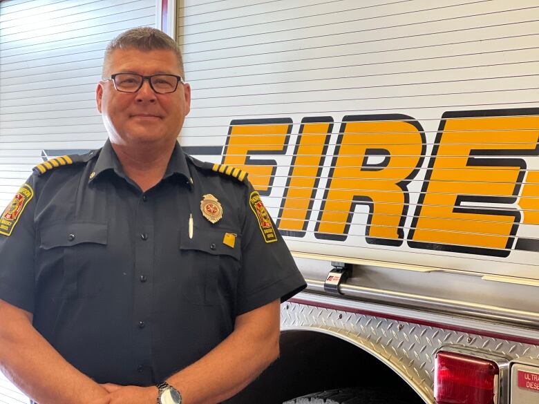 A man wearing a fire uniform and glasses standing in front of a fire truck