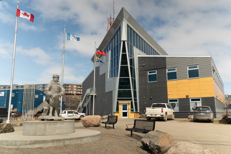 A building is seen with flags outside and a sculpture.