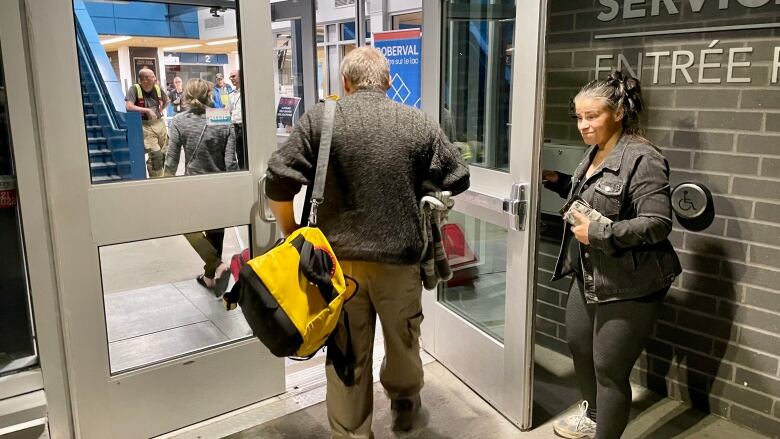 A person holds the door open for someone carrying a duffle bag 