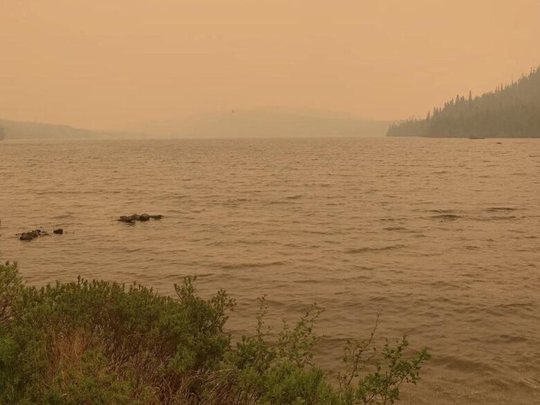 A lake overlooking mountains is obscured by smoke and haze 