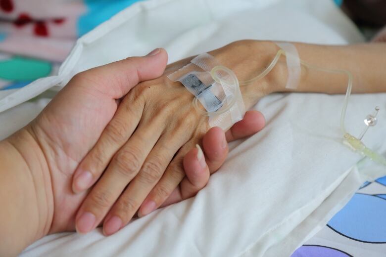 A patient's hand is being held by another person's. An IV can be seen in the patient's hand.