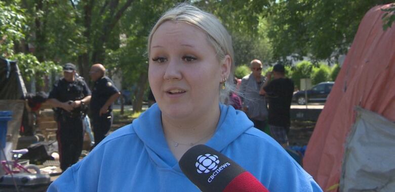 A woman with blond hair in a bun and a blue hoody is being interviewed. 