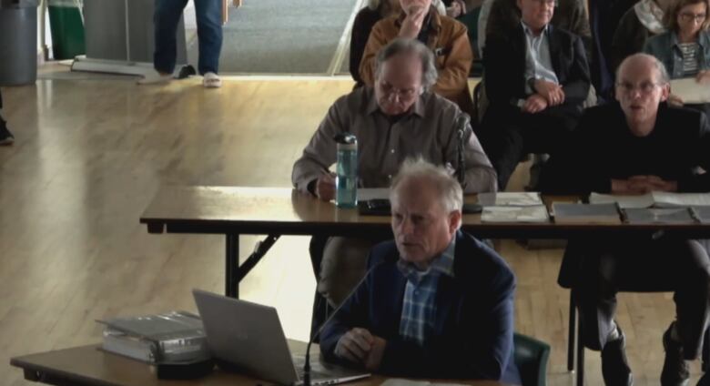 A man sits at a desk in front of a laptop during a Nova Scotia Aquaculture Review Board hearing.