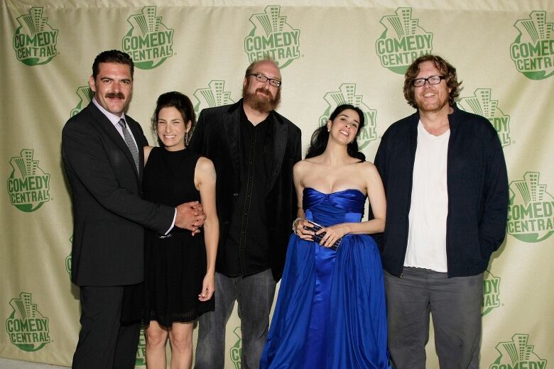 Three men and two women are shown posing for a photo at a celebrity event.