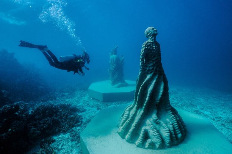 A scuba diver swims past statues anchored underwater.