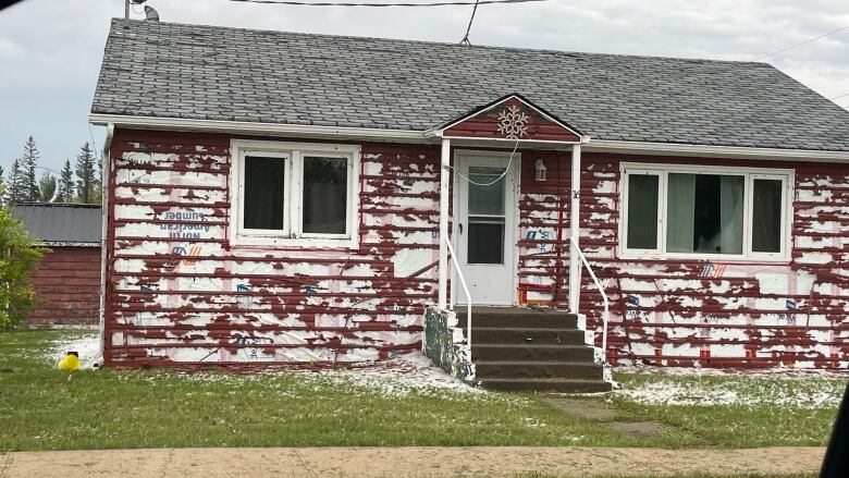 House wrap shows under siding that has numerous holes in it. Hail stones are seen on the grass surrounding the house.