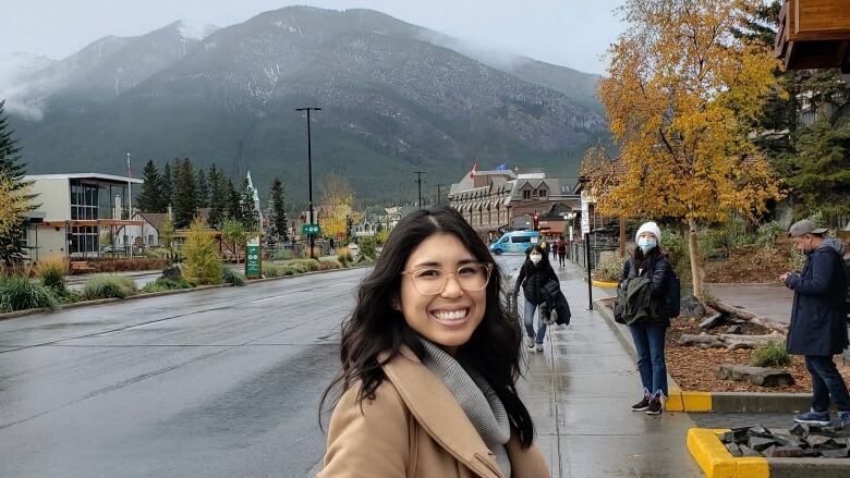 A woman turns to smile at the camera while on a street in a mountain town.