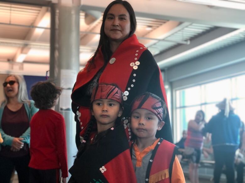 A mother and her young daughter and son dressed in Indigenous regalia.