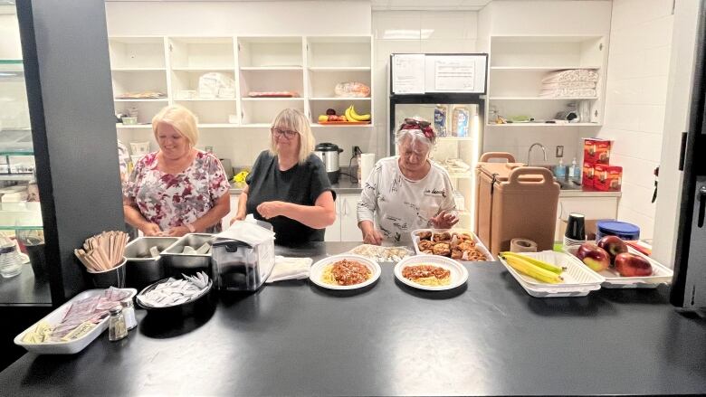 Three women stand in a kitchen.