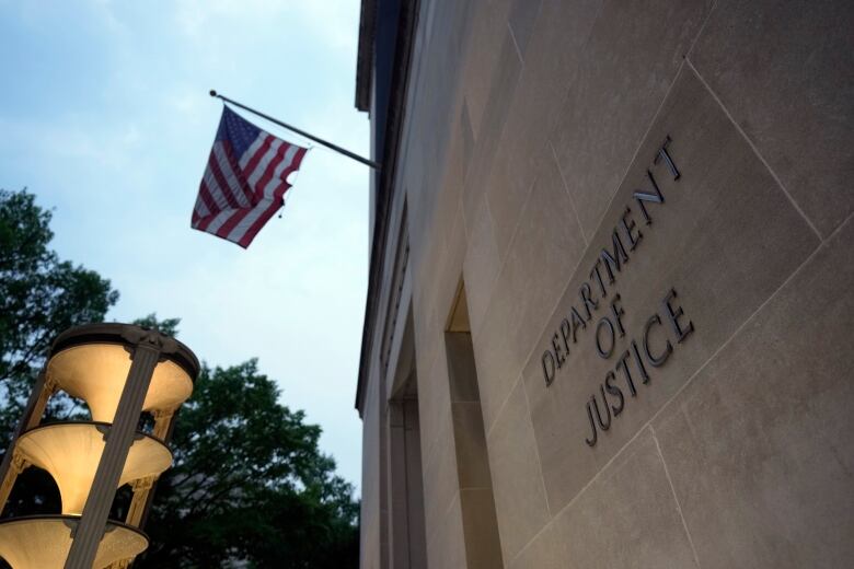 A sign on a stone building flying and American flag reads Department of Justice.