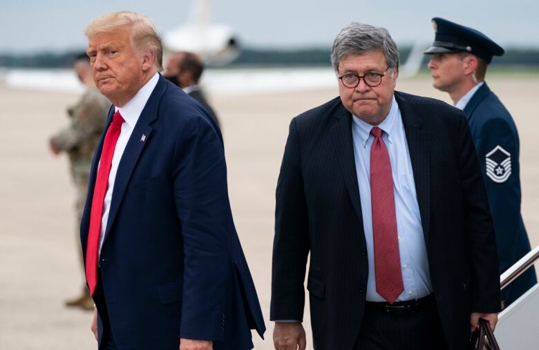 Two men wearing dark suits and red ties depart a flight on an airport tarmac. 