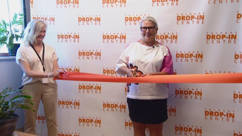 A smiling woman cuts an orange ribbon. She is wearing a white and pink shirt and black skirt. 