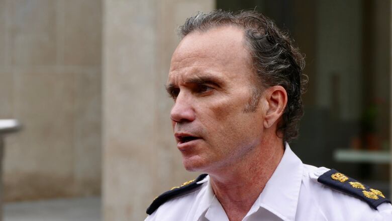 A man in police uniform speaks outdoors.