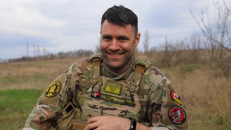 A person wearing a military uniform is shown in a field.