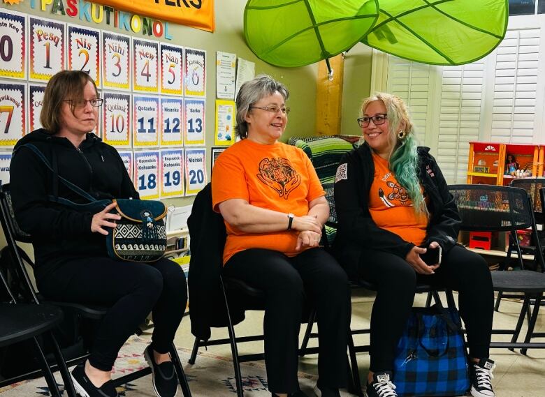 Three women sit together on black folding chairs.