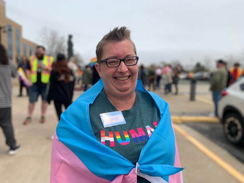 A woman wrapped in a trans flag with a crowd in the background