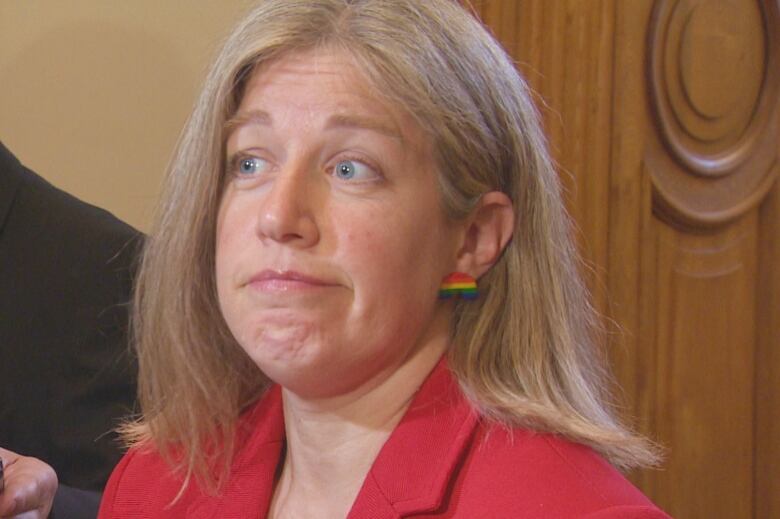 A woman with blonde hair and a red blazer wearing rainbow earring studs