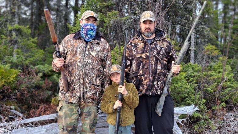 A family wearing camo carries guns as they pose in the forest 