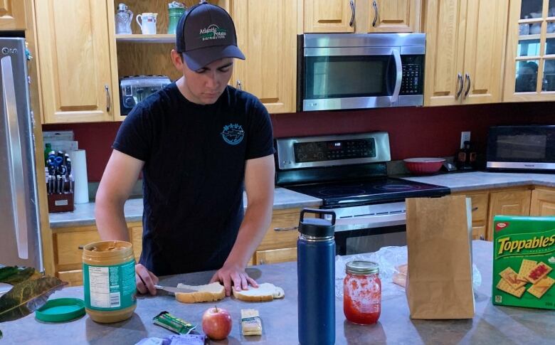 A man standing behind a counter making a peanut butter and jam sandwich