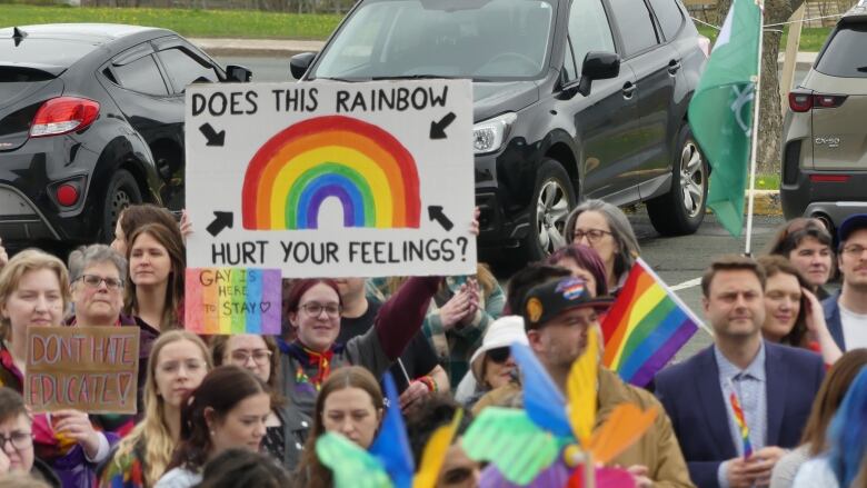 A woman in a crowd holds a sign that says does this rainbow hurt your feelings