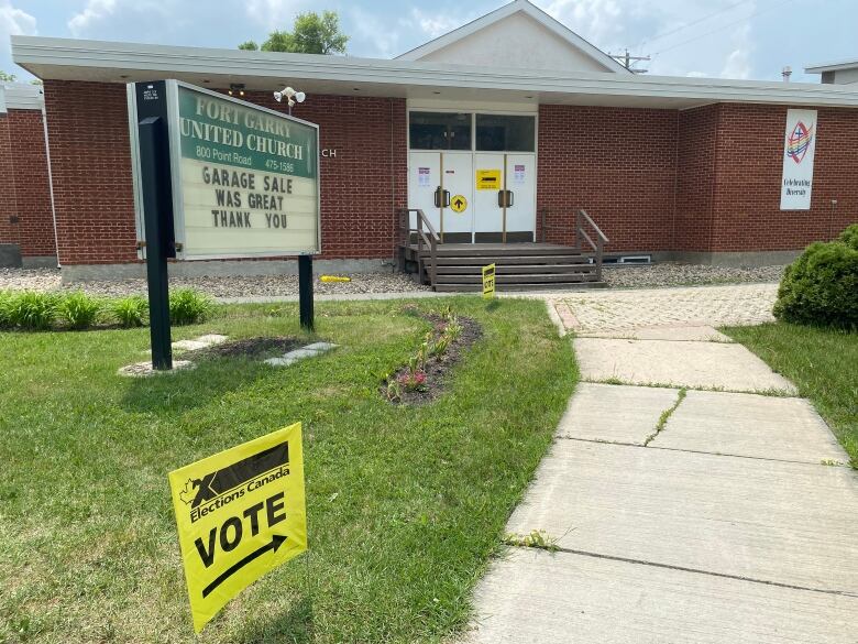 Yellow Elections Canada signs sit outside and on the doors of a red brick church building.