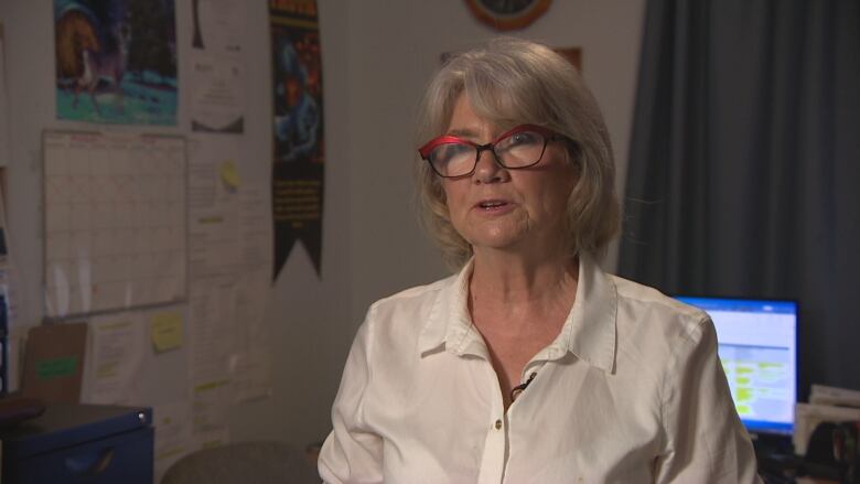 A woman with grey hair and red glasses does an interview.