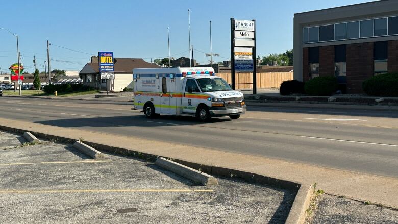 A white ambulance with neon logos travels down a road. 