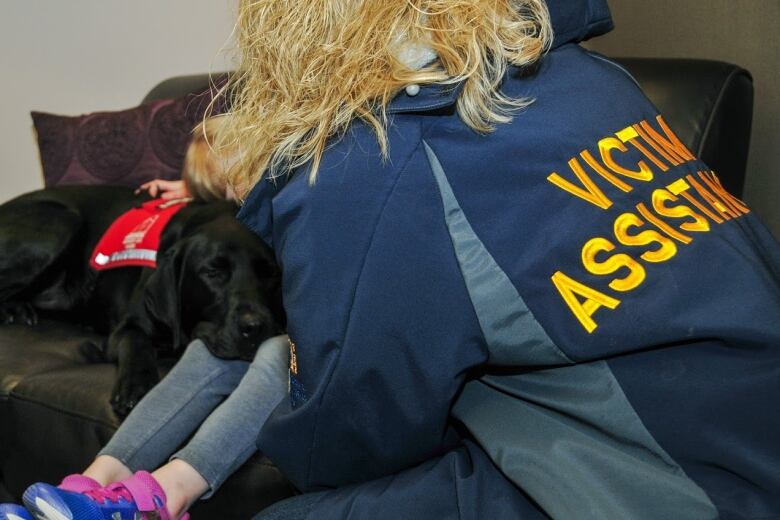 A close-up shot of a Black Labrador with a red vest, resting his head on someone's lap.