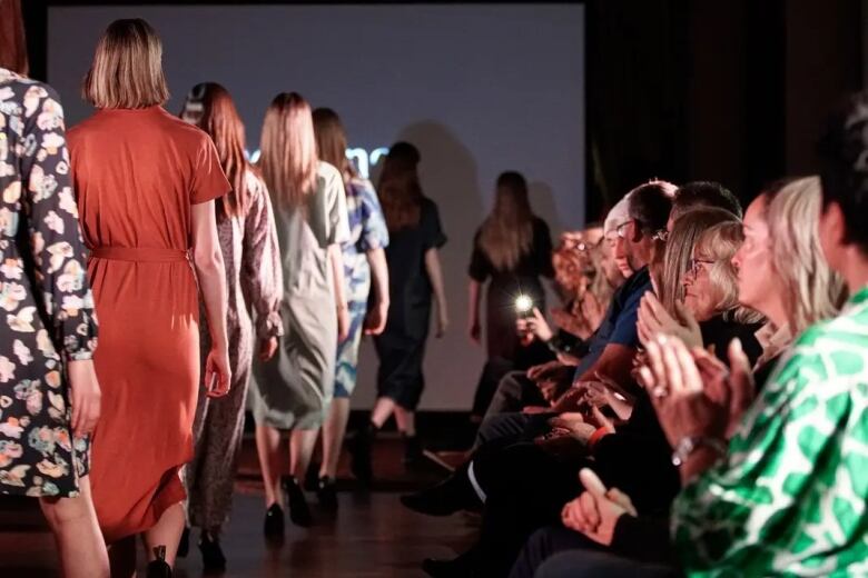 Models walk on a runway while audience members clap.