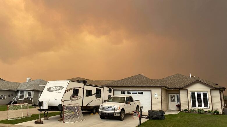 Dark orange and grey smoky skies over a house with a white truck and an RV in the driveway.