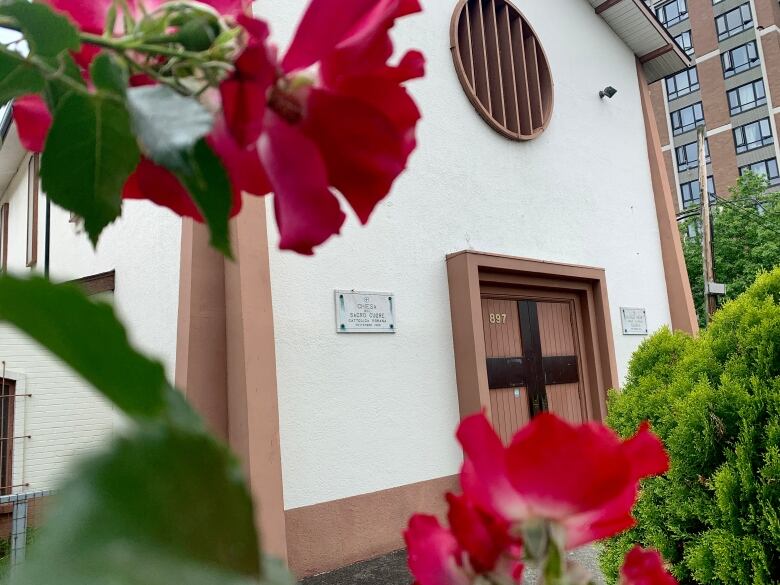 A catholic church entrance is seen with pink roses in front of it.